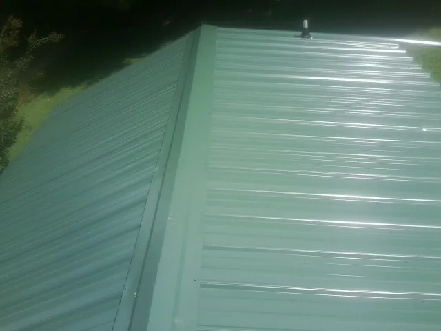 New green metal panels meeting at the ridge of a roof — Flat Roof Repair work by our crew in Davidsville