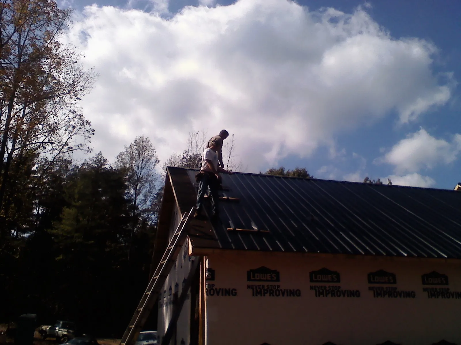 Roofer fastening dark metal panels high against a cloudy sky, from a Roof Inspection job in Davidsville