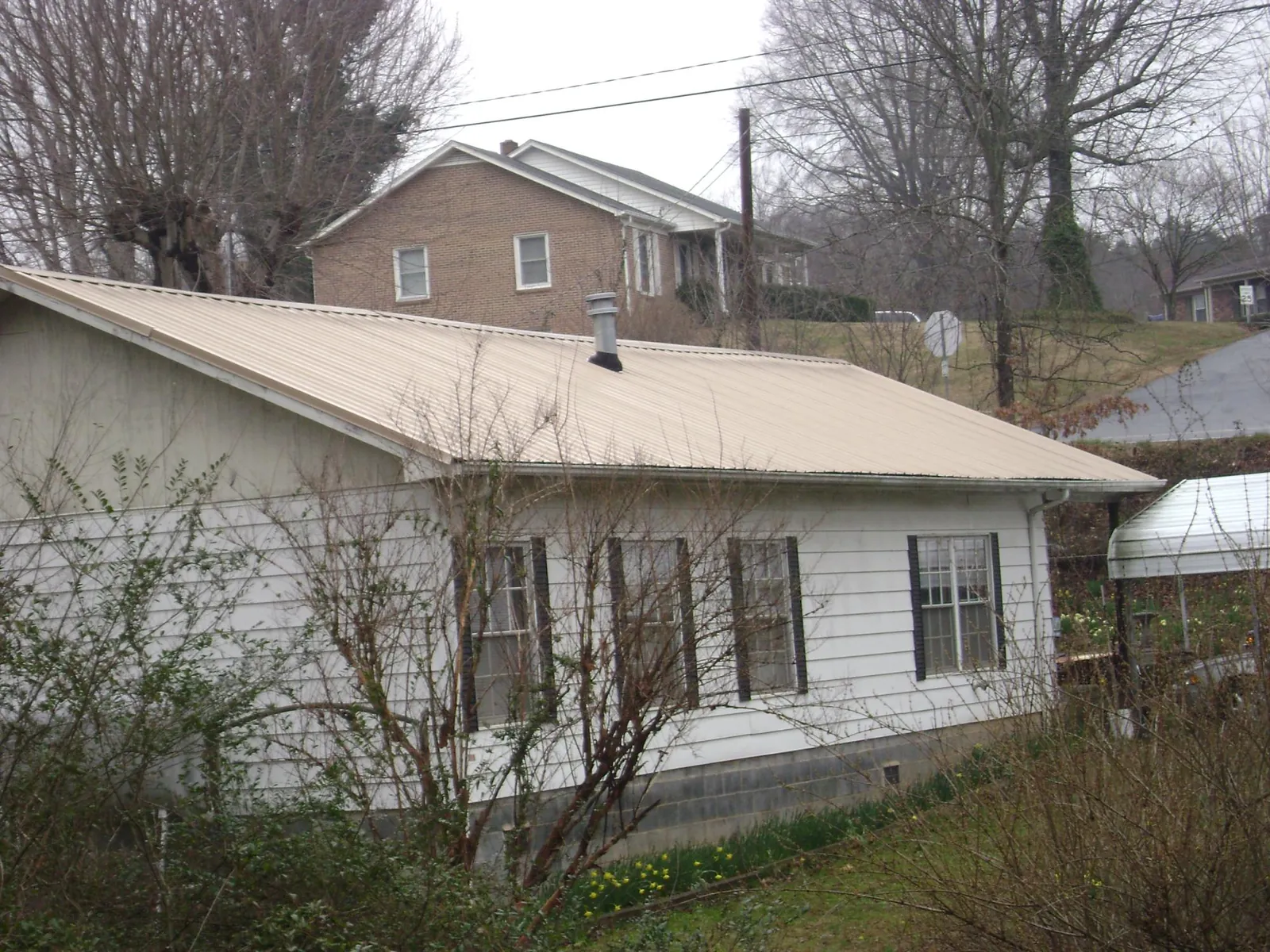 Tan metal roof on a white sided house set into a hillside — Commercial Roofing by Roofing Brothers in Davidsville